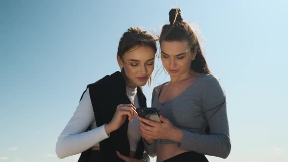 Two Athletic Women in Sportswear are Taking Break and Looking at Phone