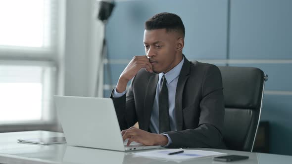African Businessman Thinking while Working on Laptop in Office