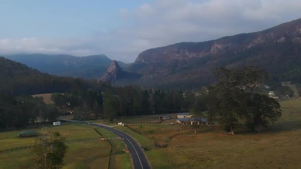 Aerial view of a country road winding through a hinterland bush valley with a pinnacle shaped mounta