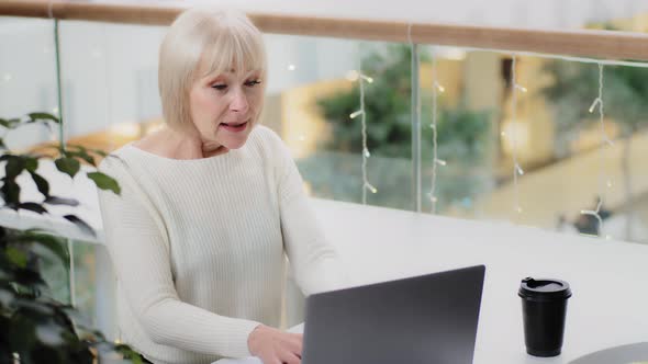 Excited Excited Middle Aged Caucasian Woman Sitting at Desk Using Laptop Intently Playing Computer