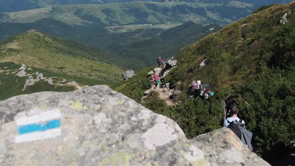 Group of Tourists and Children with Backpacks Go Down on Stone Trail in Mountain