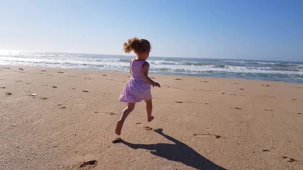 Toddler girl running on the beach towards the ocean