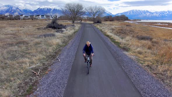 Mature, older man bicycling along a nature path with scenic, snowcapped mountains in the distance -