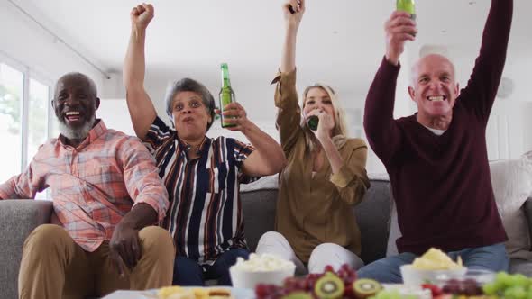 Two diverse senior couples sitting on a couch watching a game drinking beer