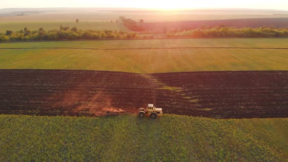 Top View Tractor with Harrow System Plowing Ground on Cultivated Farm Field Pillar of Dust Trails