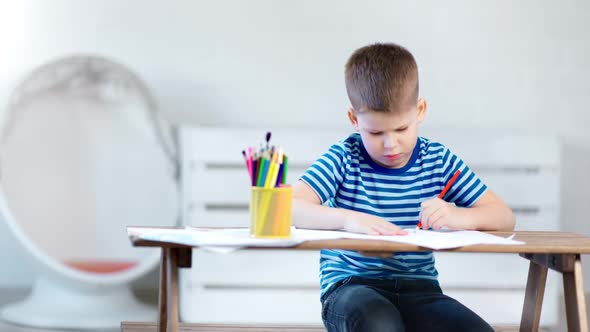 Pensive Little Kid Boy Concentrated Writing on Paper Using Colorful Pencil at White Modern Interior