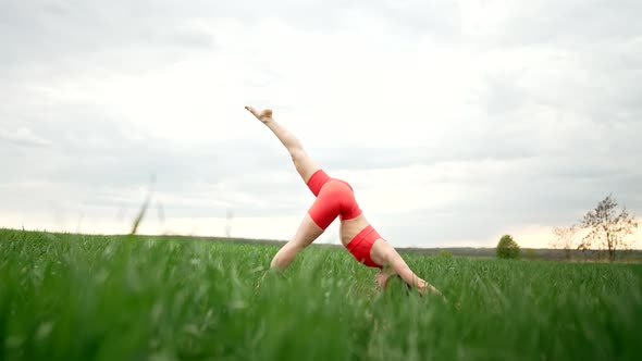 Young Woman in Orange Sports Wear Practicing Yoga in Green Field