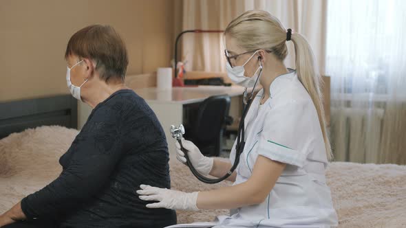 Family doctor examining senior woman at home. Medical consultation. Listen with a stethoscope