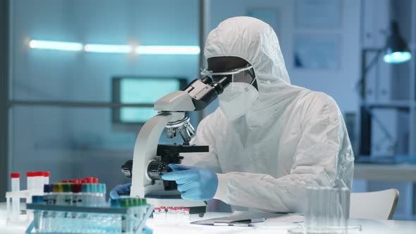 Black Doctor in Protective Suit Working with Microscope in Lab