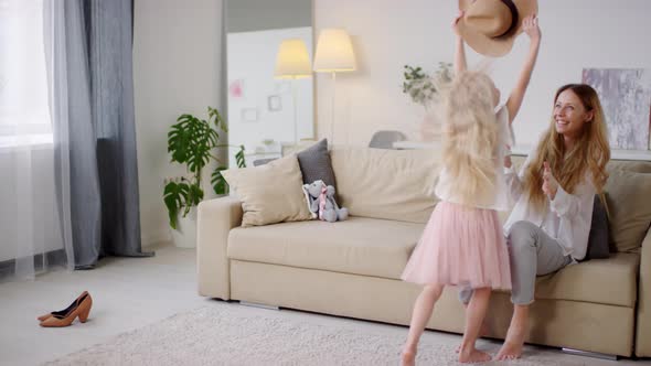 Adorable Girl Putting Hat on Mother and Hugging her