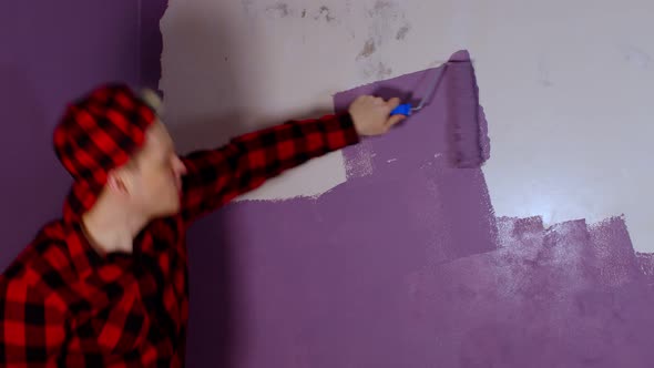 Close Up of Young Man Dancing and Painting Wall in Purple Colour with Roller