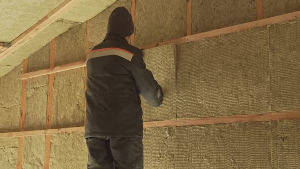 Man laying insulation in a wall under roof