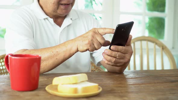 Senior Asian Man Using Smartphone During Breakfast