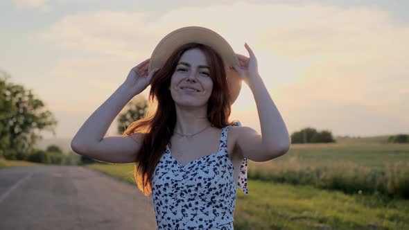 Beautiful Ginger Woman Puts on a Straw Hat and Playfully Smiles Outdoor