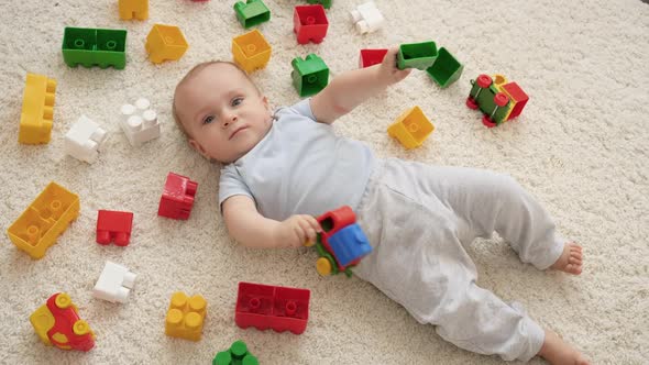 Little Smiling Baby Boy on Carpet in Playroom Covered with Colroful Toys Bricks and Blocks