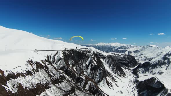 Beautiful epic landscape of high altitude mountains, bright coloured paraglider parachute flies down