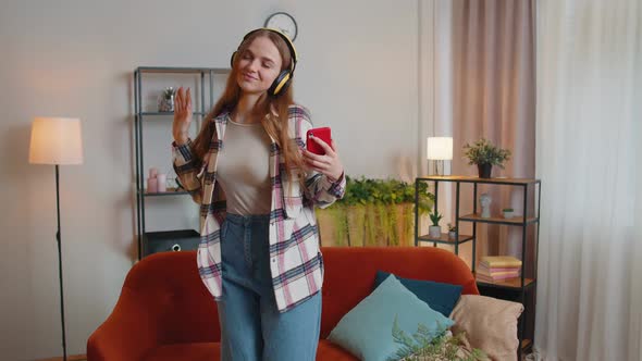 Overjoyed Young Woman in Wireless Headphones Dancing Singing on Cozy Couch in Living Room at Home