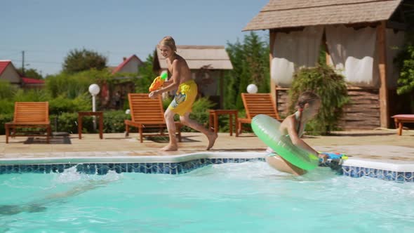 Four Caucasian Kids Playing Near Pool with Water Pistols and Inflatable Tubes in Slowmotion