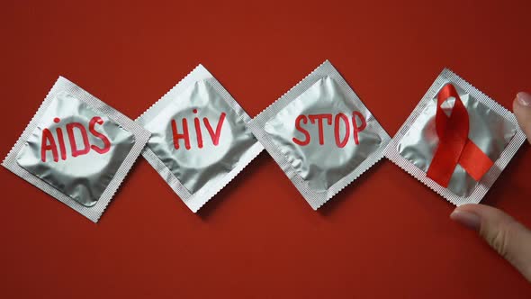 AIDS HIV Stop Words and Red Ribbon on Condoms on Red Background, Prevention