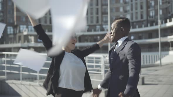 Multiracial Partners Throwing Up Documents and Hugging in Sunlight. Portrait of Happy Caucasian