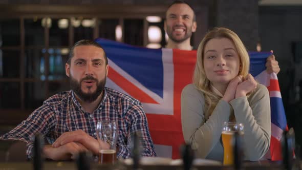 Men and Woman Watching TV in Pub Supporting National British Team on Championship with Flag