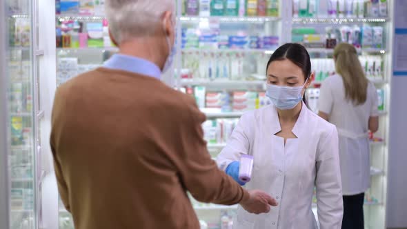 Young Asian Woman Taking Temperature of Caucasian Senior Man in Pharmacy at Entrance