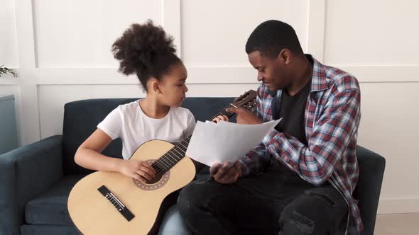 AfricanAmerican Man Teaching His Little Daughter to Play Guitar at Home