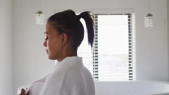 Mixed race woman standing in bathroom taking bathrobe off