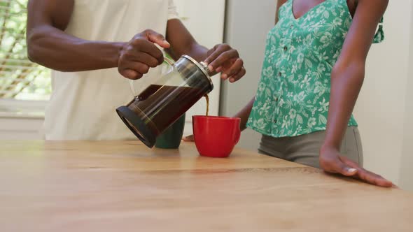 Midsection of african american couple in kitchen pouring coffee from cafetiere