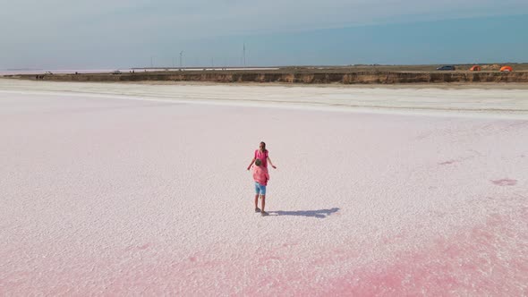 Man Holds His Girlfriend on Hands Having Fun Standing on Shore of Beautiful Colorful Pink Lake