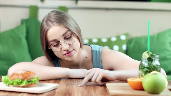 Smiling Funny Young Woman Playing Fingers on Table Choosing Between Healthy and Unhealthy Food