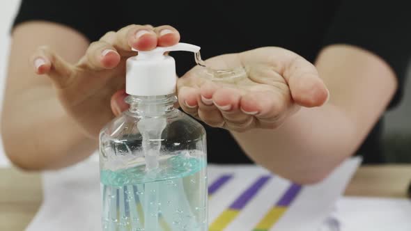 Business woman cleaning hands with sanitizer alcohol gel while working on her desk.