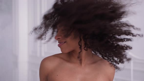 Happy Black Woman Looks at Camera Shakes Her Hair in White Room and Smiles