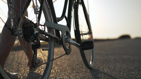 Closeup Bicycle Wheels Rolling in Slow Motion in Sunrays with Legs of Young Slim Caucasian Woman