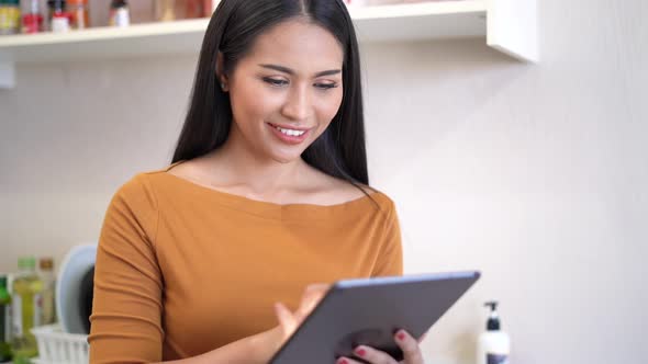 Young woman relaxing standing in kitchen and using digital tablet.