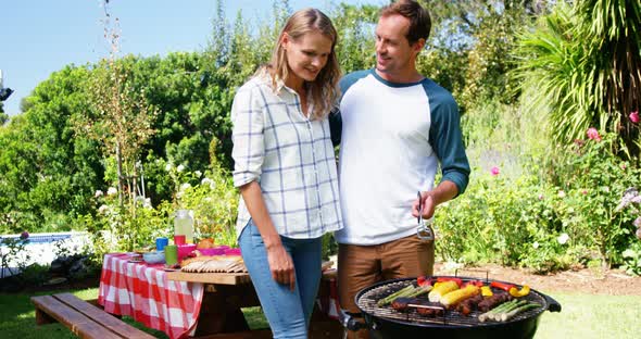 Couple grilling meat and vegetables on barbecue