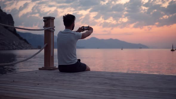 Selfie At Sunset Over Sea In Vacation Holiday.Man Sitting On Embankment And Taking Selfie On Sunset.