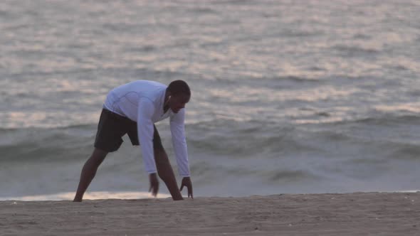 A young man runner  stretching on the beach at sunset.