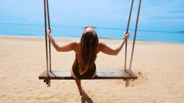 A Young Woman in Green Swimming Suit Swinging on a Swings on the Beach and Having a Rest