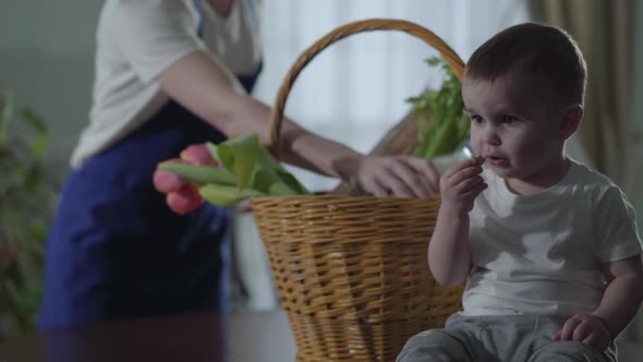 A Little Boy Sits Near the Basket on the Table and Eats