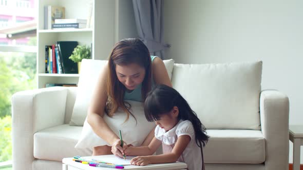 Young mother teaching cute daughter drawing on paper