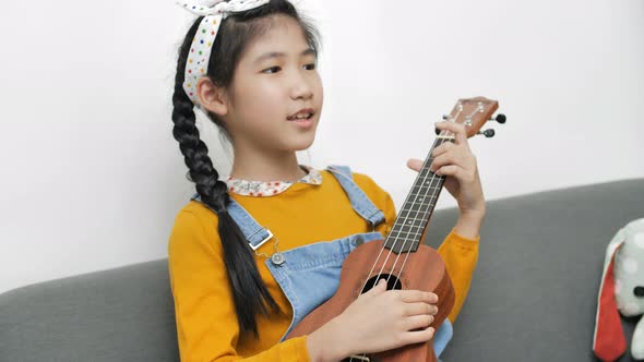 Little Asian child playing ukulele and singing a song