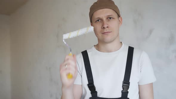 Man Construction Overalls Happily Shows Paint Roller To Camera