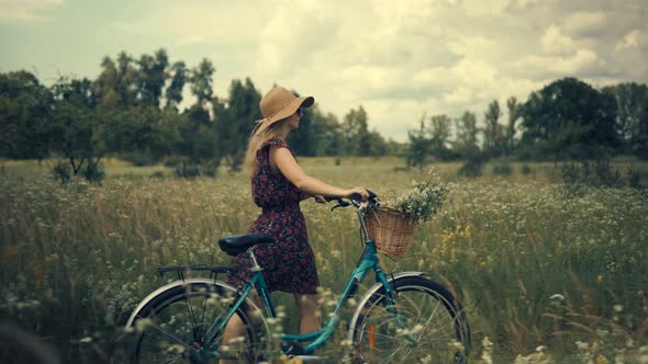 Girl In Sunglasses And Dress.Tourist Girl Relaxing On Countryside Wildflower Field.Woman Cyclist.