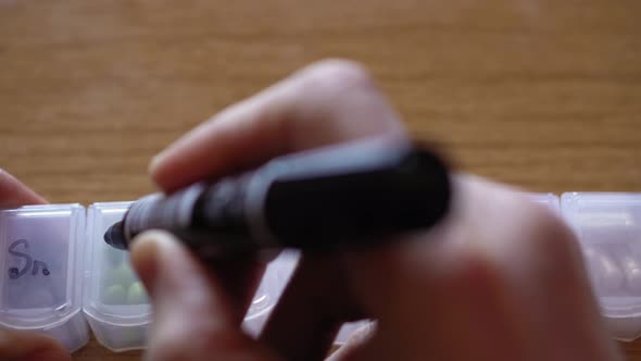 Close Up of Male Hand Fingers Marks Cells with Black Marker for Days of Week in Plastic Pill