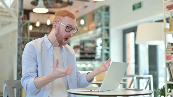 Redhead Man Celebrating Success on Laptop in Cafe 