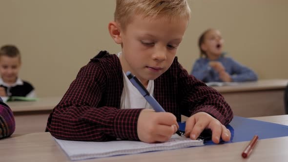 Closeup of a Little Boy Sits at a Desk in School and Writes in a Notebook