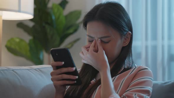 Exhausted Asian young woman hurt eye while using mobile phone at night.