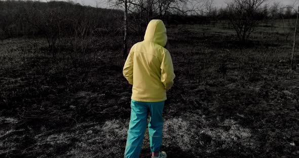 Teenage homeless girl in colorful Ukrainian clothes walks on a burnt field