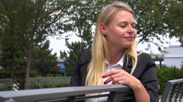 A Young Beautiful Businesswoman Sits on a Bench and Looks Around in a Park - Closeup